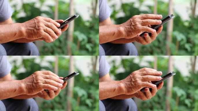 老人的手用左手拿着黑色智能手机，用右手手指触摸屏在花园里给家人发短信，家里有绿色的环境。在线，互联网