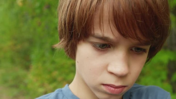 特写脸和眼睛少年男孩在绿色的夏日树木背景。肖像男孩少年在户外看东西。