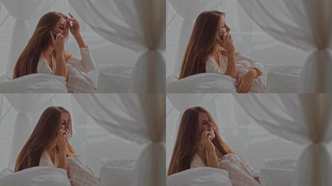 在电话里聊天的女孩。年轻女子穿着睡衣坐在床上，和她的朋友聊天。肖像视图。