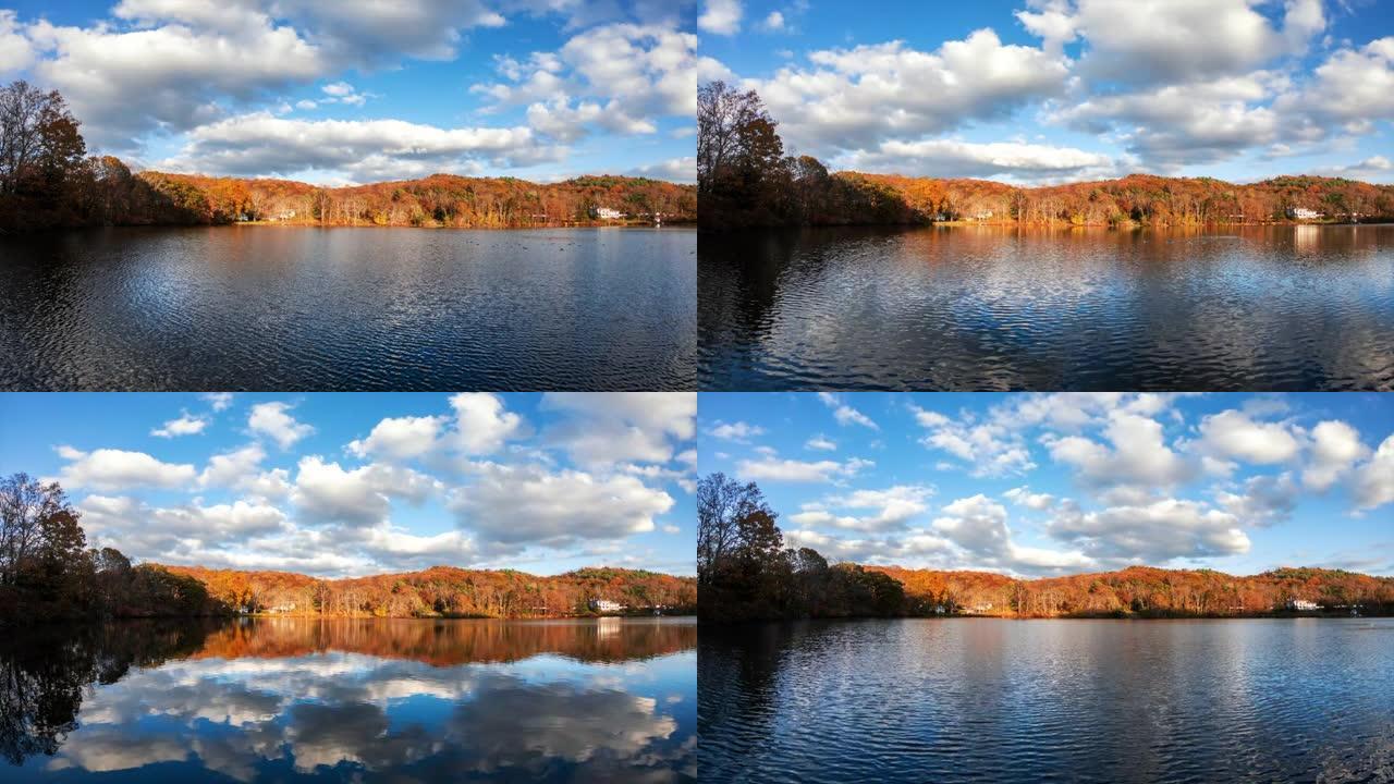 白色浮肿的云朵划过天空，在秋天的树叶环绕的湖中反射。