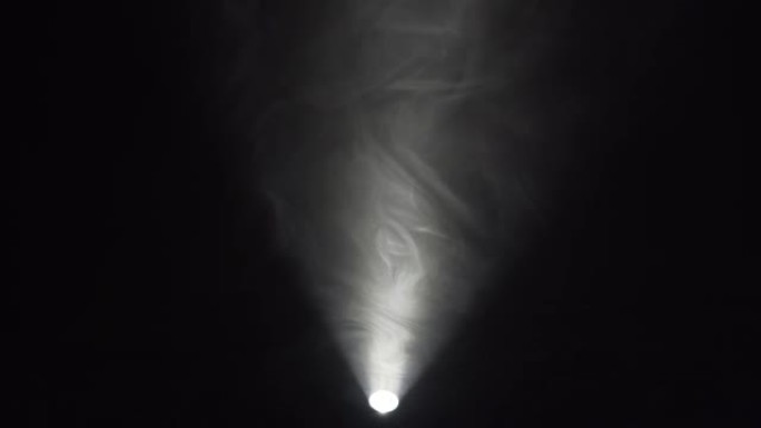 在手电筒的光线下，黑暗背景上的雾、云或雾。运动中的烟雾或蒸气4K。文本或设计空间