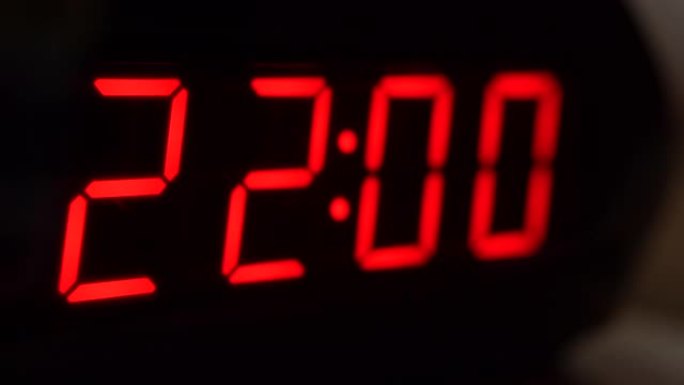 黑色数字时钟屏幕的特写显示22.00。黑色背景上闪烁的数字。现代定时器和红色霓虹灯、电气设备和现代技