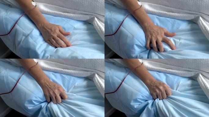 生病的老年患者的手在医院挤压床单，痛苦不堪