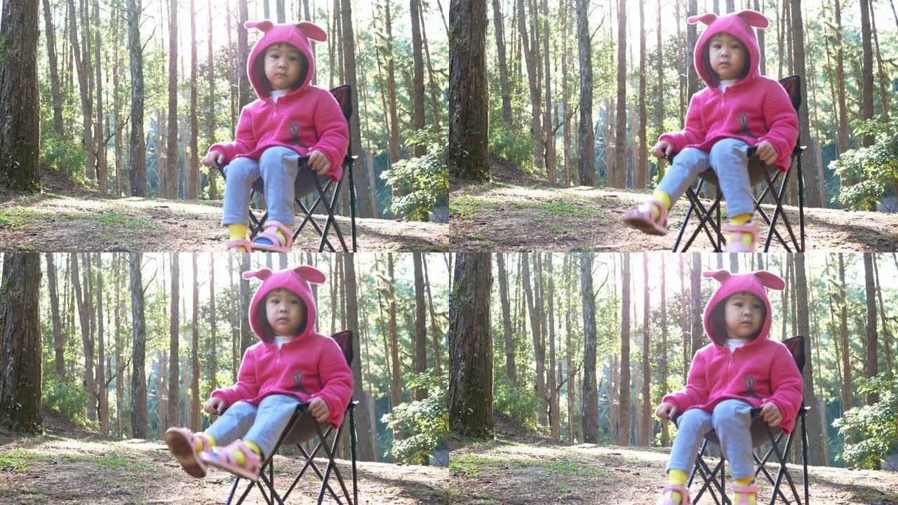 亚洲小女孩和家人一起去松树林露营时坐在椅子上。儿童户外活动和大自然冒险的概念。