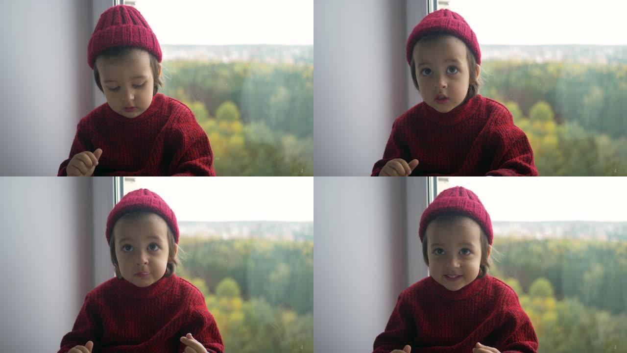 穿着红色毛衣和针织帽的男孩孩子坐在一个大白色窗户上