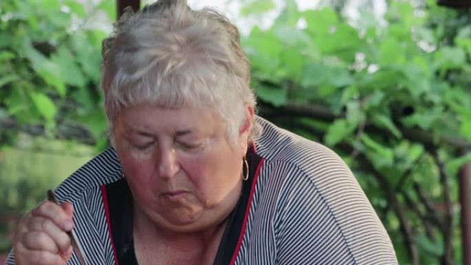 一位超重的老年妇女用勺子吃户外蔬菜沙拉，看上去很沉思