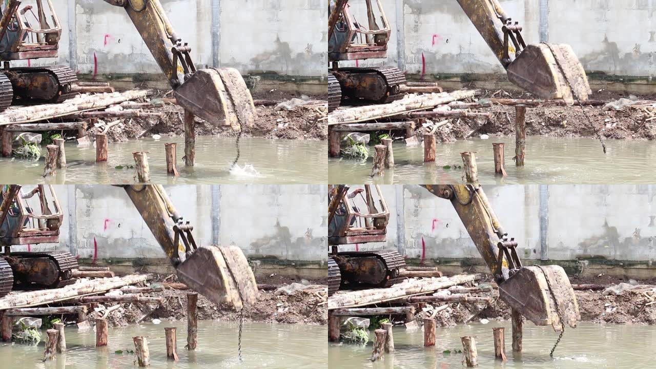 挖土机或挖土机在运河中挖斗地面用木基杆保护河岸塌陷的路堤施工现场的过程。