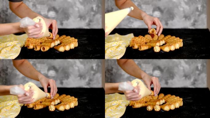 女人的手将奶油倒入牛角卷的两端。用奶油做泡芙卷的女人。