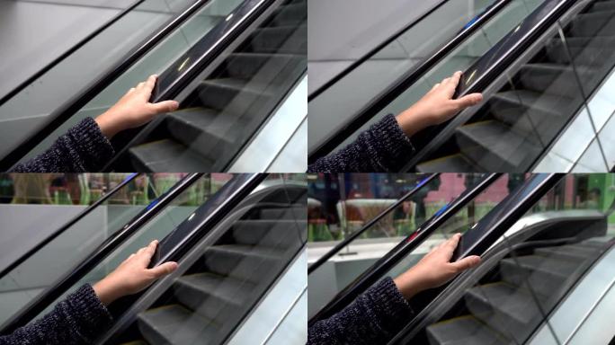 骑透明自动扶梯并握住扶手的女人的手的特写。向上运动。概念。4K。