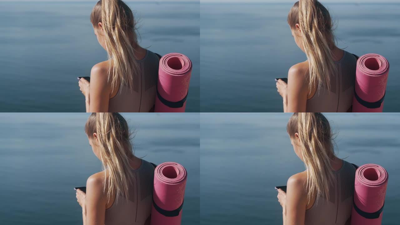 运动员女孩手里拿着手机的背面视图，背景是海洋