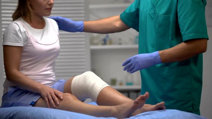 创伤专家在检查过程中检查弹性包裹的女性膝盖，创伤