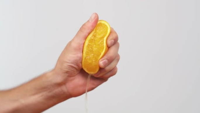 用手挤出新鲜的橙子。柑橘汁从果肉和水滴中排出。孤立，在白色背景上