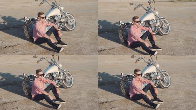 日落时，年轻时尚的摩托车手坐在沙漠路上的摩托车上