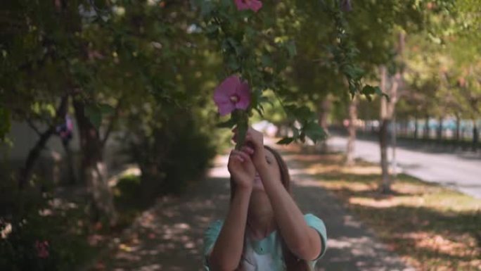 一个漂亮的年轻女孩嗅着并触摸着紫色的芙蓉花。