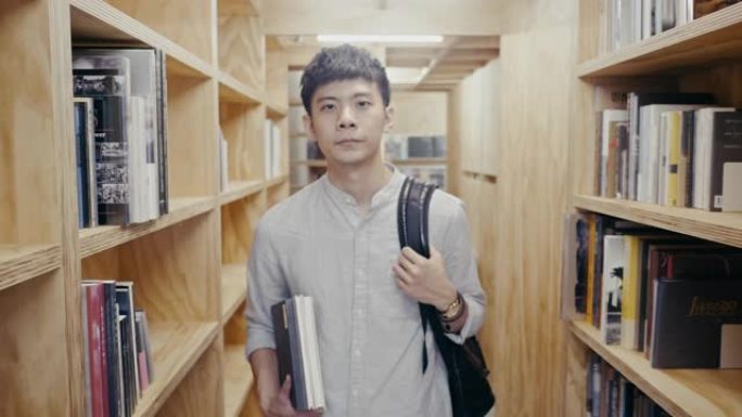 一名年轻的亚洲男学生在书架之间行走的肖像 (慢动作)