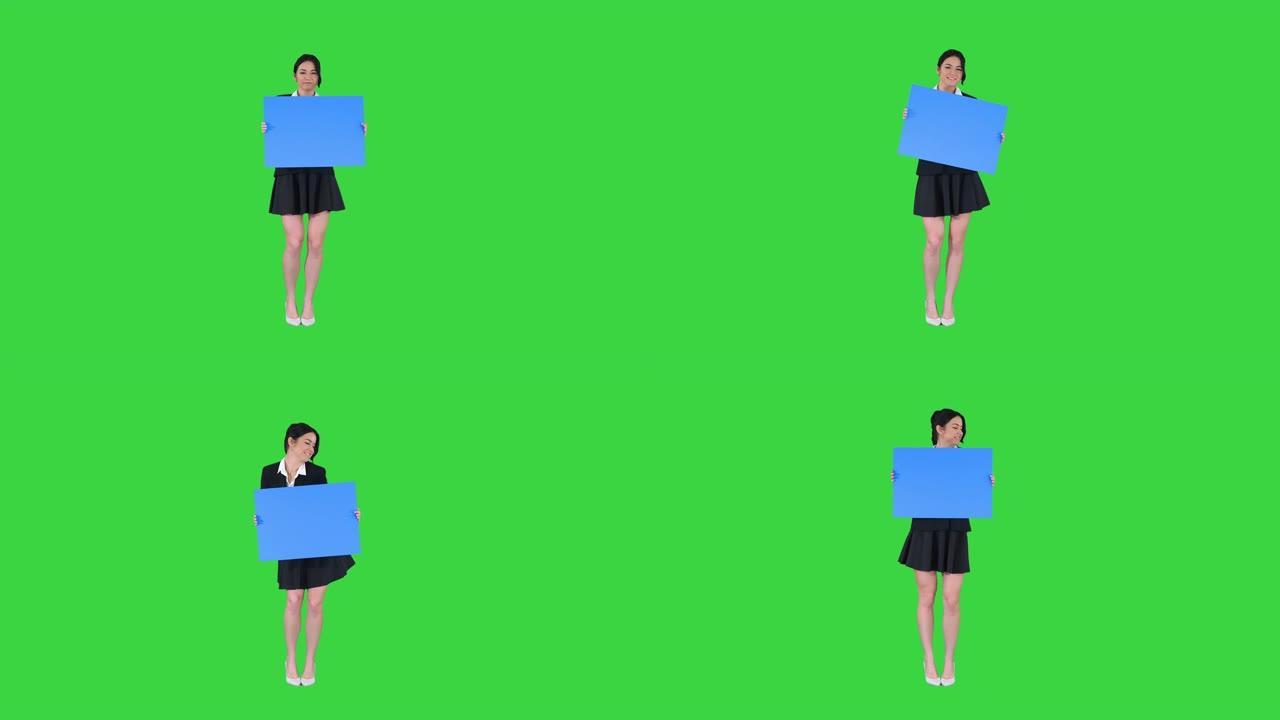 一个时髦的女人在绿屏上跳舞并拿着空海报，蓝色模型