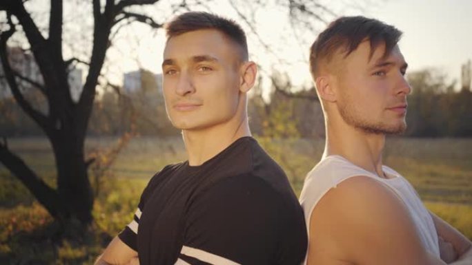 两个年轻的高加索健美运动员站在阳光下看着相机的特写脸。英俊强壮的运动员在秋季公园度过时光。健康的生活
