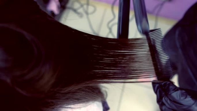 美发师在美容院用发钳直发美女的深棕色头发。