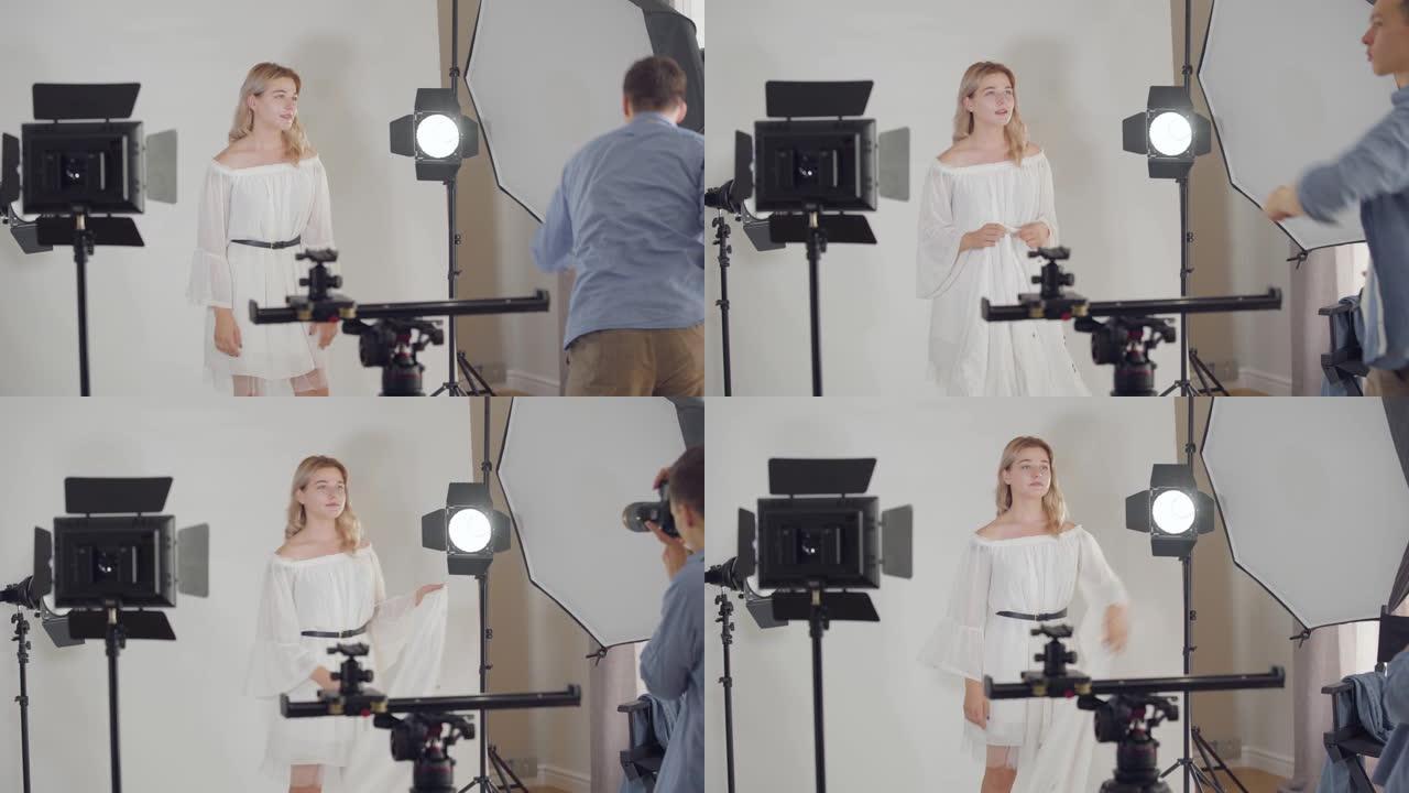 摄影师在摄影棚里拍摄漂亮女孩在白色背景上摆姿势的照片。