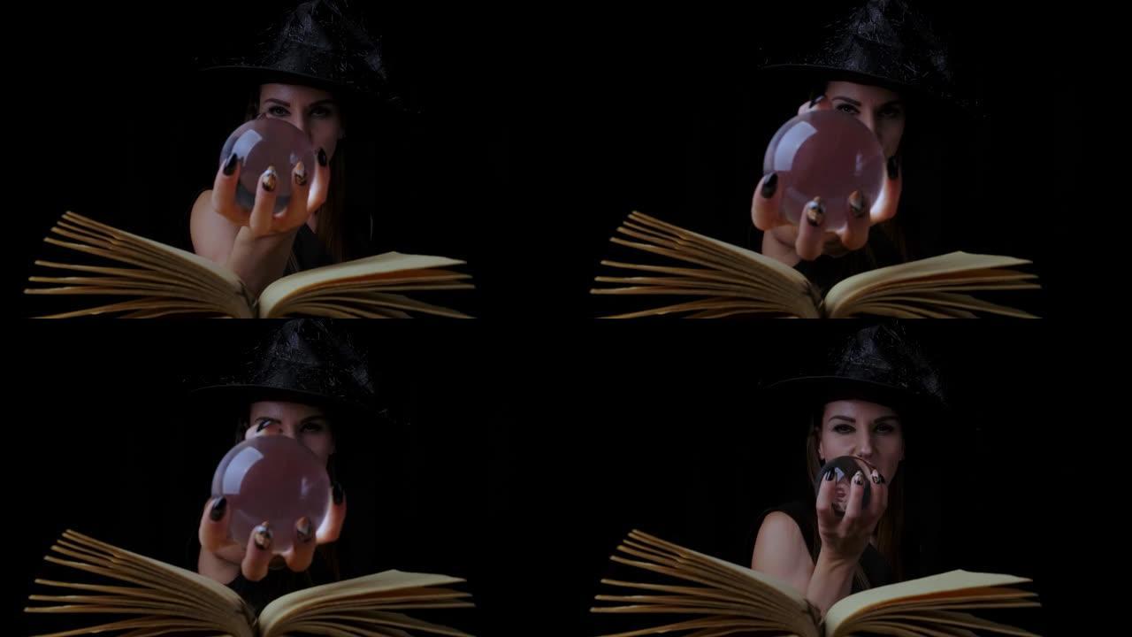 穿着黑色女巫服装和帽子的美丽性感女人，手里拿着一个透明的魔术球，让人联想到。特写。万圣节节日派对