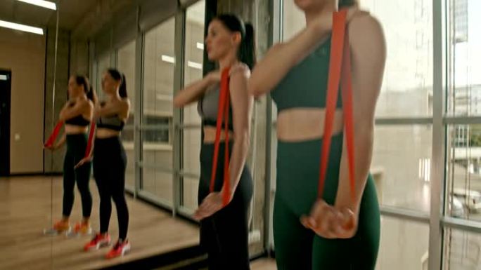 两名穿着运动服的健康女性站在工作室里，用伸缩带训练她们的手。