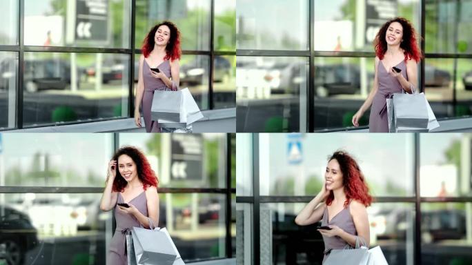 迷人的微笑红发女孩与智能手机享受购买步行商场玻璃背景