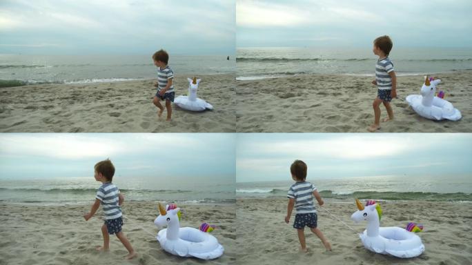 快乐的小男孩带着独角兽充气戒指在沙滩上奔跑