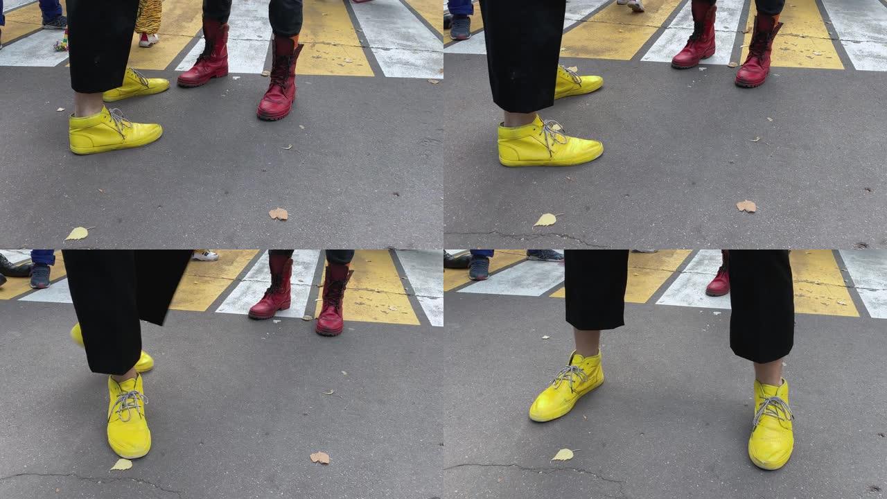 小丑的腿和脚穿着彩色有趣的黄色和红色靴子，在柏油路上互相玩耍