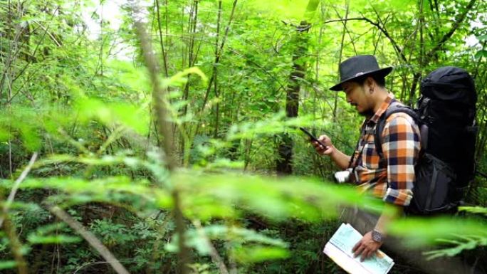 在天然森林中使用智能手机用背包平移男子旅行者的照片