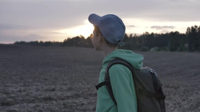 带着背包的旅行男孩在日落时走在户外