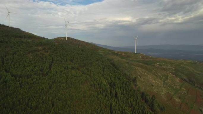 跳伞运动员飞过覆盖着绿树的山顶上的风力发电机