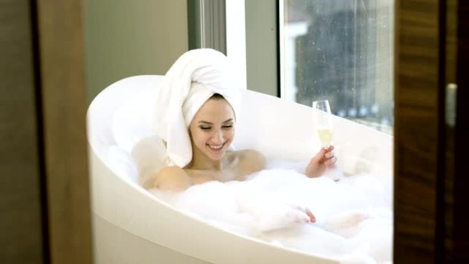 快乐的年轻女子，洗泡泡浴，在浴室喝香槟。4 k