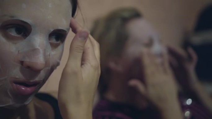两名妇女在脸上涂上日本化妆品薄纸面膜，使脸上的面膜光滑。