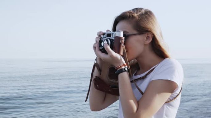 特写女人用复古相机拍照，在日落时拍摄美丽的大海。享受旅游生活方式度假观光。她站在海滩上。侧视图。