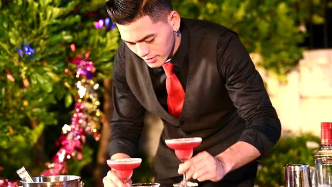 穿着黑色正装和红色领带的迷人英俊的亚洲男性调酒师混合在兼职生日快乐活动中作为艺人制作鸡尾酒。职业和人