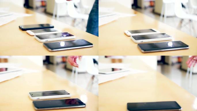 注意桌子上的桌子连续摆放几部手机，年轻人的手从桌子上拿起手机径向相机跟踪