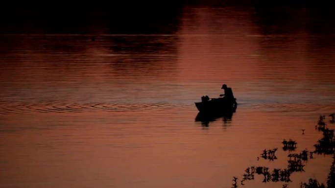 黄昏时在船上寻找鱼的剪影人。