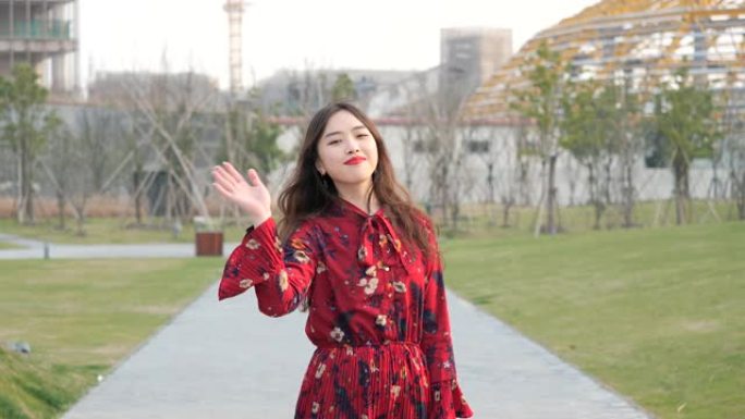 一个穿着红色连衣裙的漂亮中国女孩的肖像转过身来，挥舞着她的手向她的朋友道别，4k镜头，慢动作。