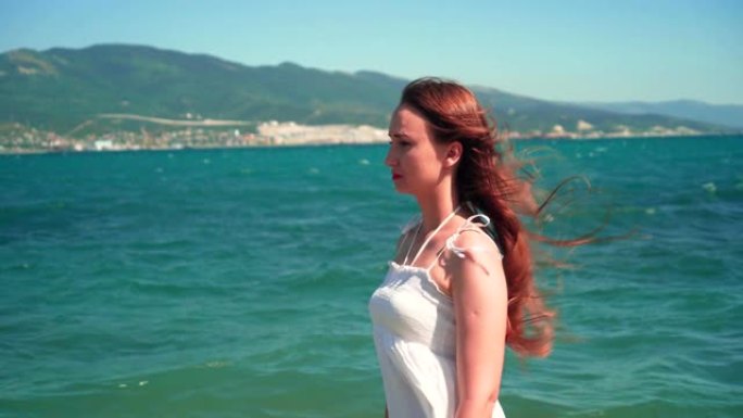 一个穿着白色沙滩装的女孩沿着海边散步。一个光着脚的漂亮女孩沿着海边散步。
