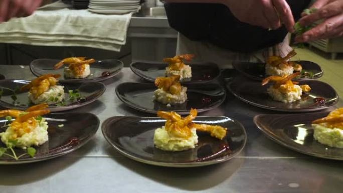大虾意大利调味饭由厨房厨师在盘子里准备和装饰。我们只能看到厨师的手把开胃菜放在盘子上-特写-烹饪概念