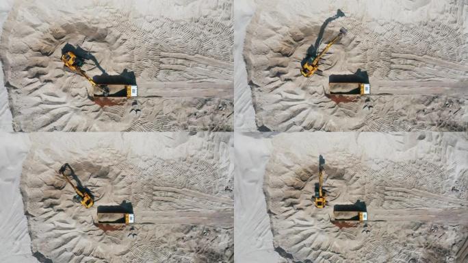 露天采石场推土机将沙子装载到空自卸车中的鸟瞰图。