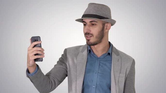穿着休闲服的有魅力的男人帽子潮人风格记录vlog或在渐变背景上进行视频通话