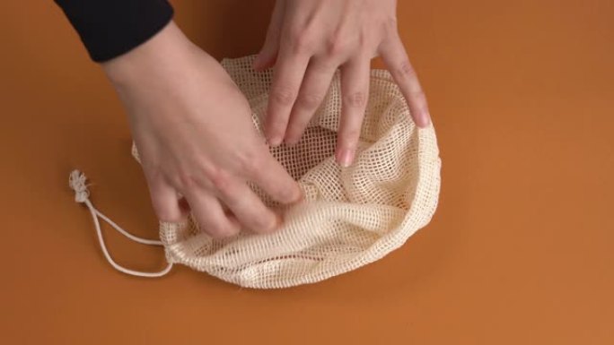 将棉网购物袋放在橙色表面上的手的特写镜头。环保