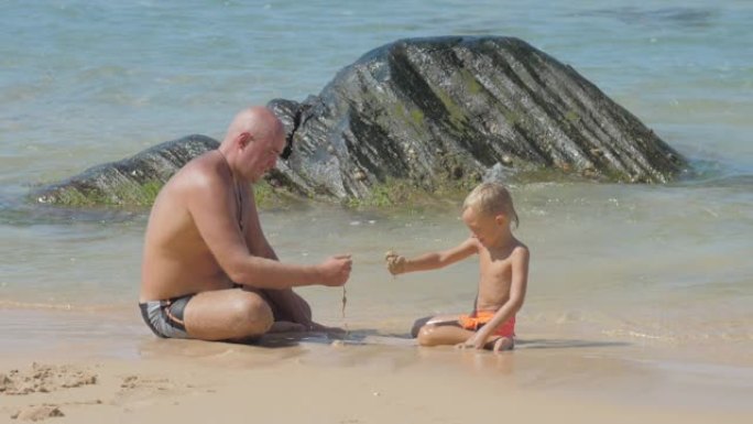 爸爸和可爱的男孩坐在冲浪线上玩湿沙
