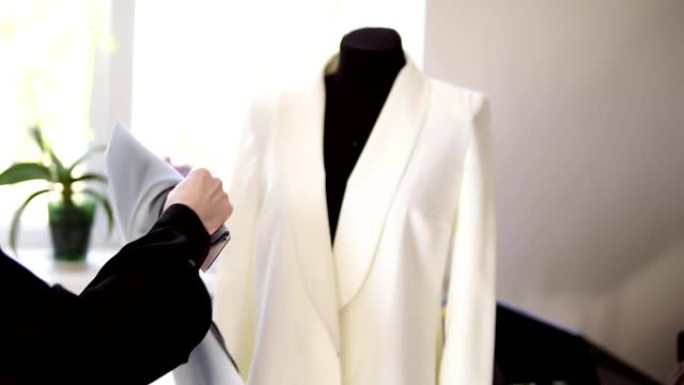 一位身份不明的创意裁缝在她工作室的假人上的白色夹克上尝试不同颜色的织物样品来缝制衣服。时装设计师准备