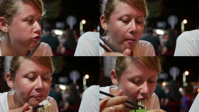女人在亚洲夜街食品市场用筷子吃鱼和米粉。特写