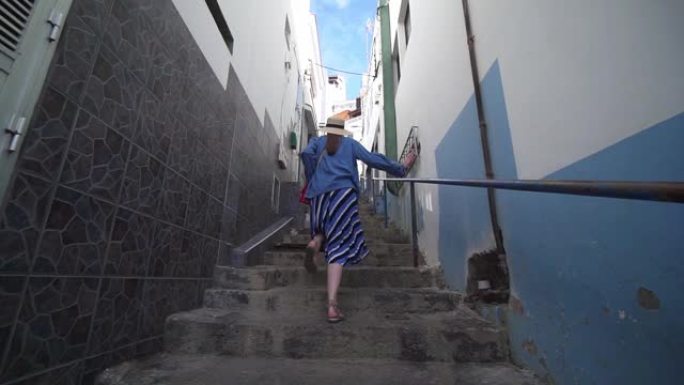 时尚的女人在西班牙古城的一条非常狭窄的街道上跑上楼梯。一名游客在西班牙特内里费岛埃尔普雷斯市散步