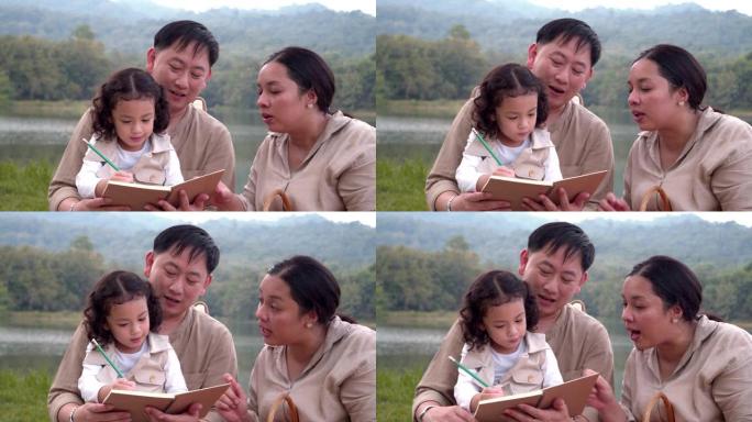 亚洲家庭父亲母亲和女儿在阳光明媚的夏天在公园的自然森林里露营和玩耍。父亲教写信。4k慢动作镜头。