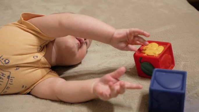 可爱的宝贝很悲伤。五个月大的孩子的肖像，穿着黄色衬衫，躺在米色的毯子上，他玩一个红色的立方体，他很难