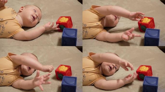 可爱的宝贝很悲伤。五个月大的孩子的肖像，穿着黄色衬衫，躺在米色的毯子上，他玩一个红色的立方体，他很难
